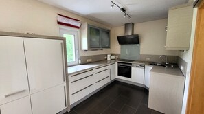 Cozinha compacta com armários brancos, forno embutido, lava-louças e janela com vista para o verde.