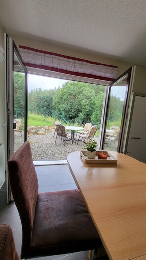 Quarto com uma mesa de madeira, um banco acolchoado marrom e vista para área externa com mesa e cadeiras.