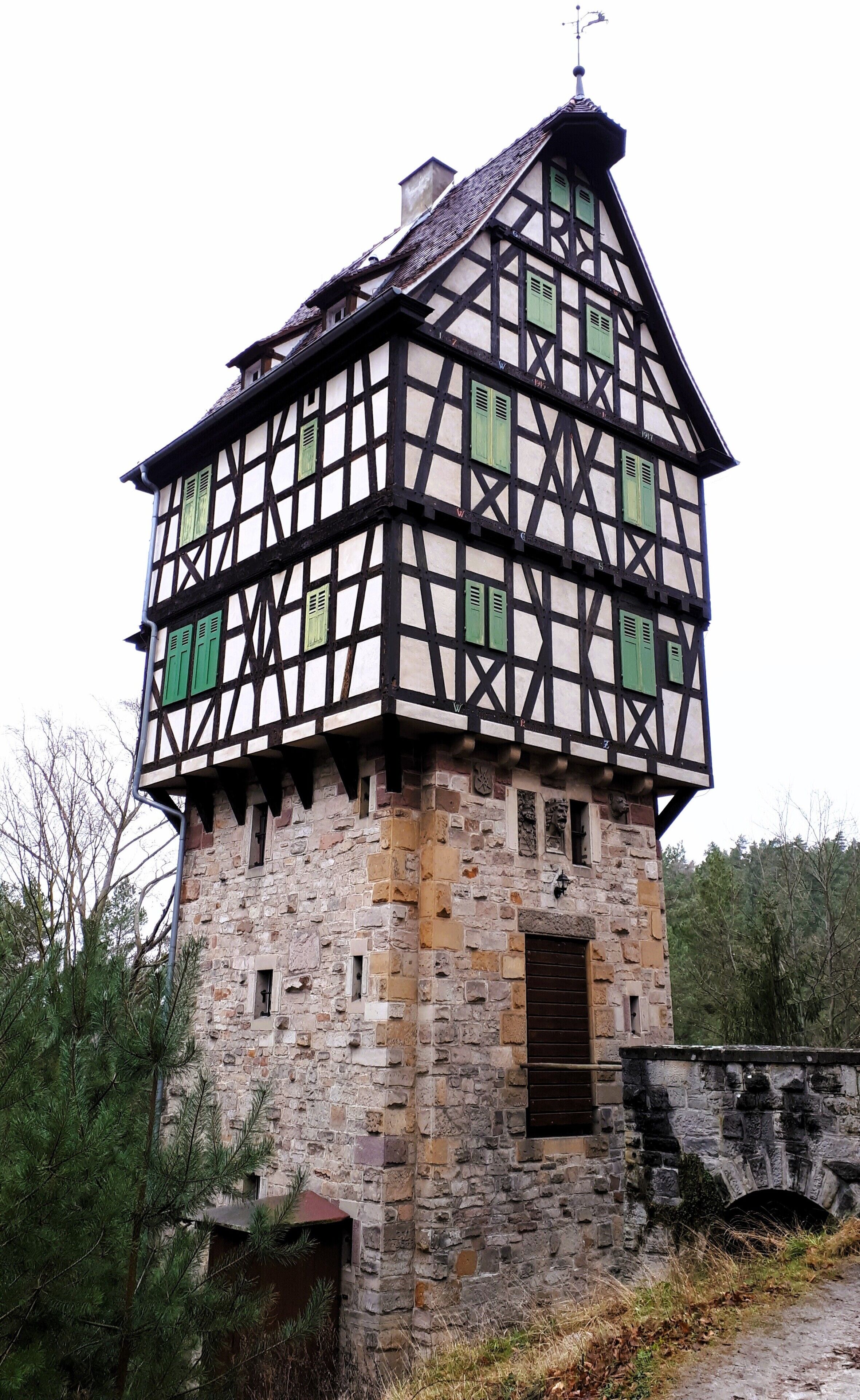 Un edificio tradicional con entramado de madera, base de piedra y numerosas ventanas con contraventanas verdes.