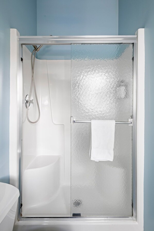 Une douche fermée par des parois de verre, avec une serviette blanche suspendue à un porte-serviettes.