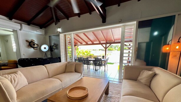 A living room with two beige sofas, a wooden coffee table, and a grill in the background. - Villa Simeon Saint Francois Avec Piscine Privee ET Jacuzzi Proche Plage Tarif Light (Saint-François)