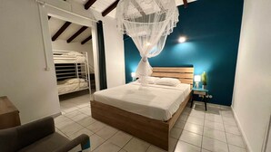 A bedroom with a wooden bed, a nightstand, a chair, and a bunk bed in the background. - Villa Simeon Saint Francois Avec Piscine Privee ET Jacuzzi Proche Plage Tarif Light (Saint-François)