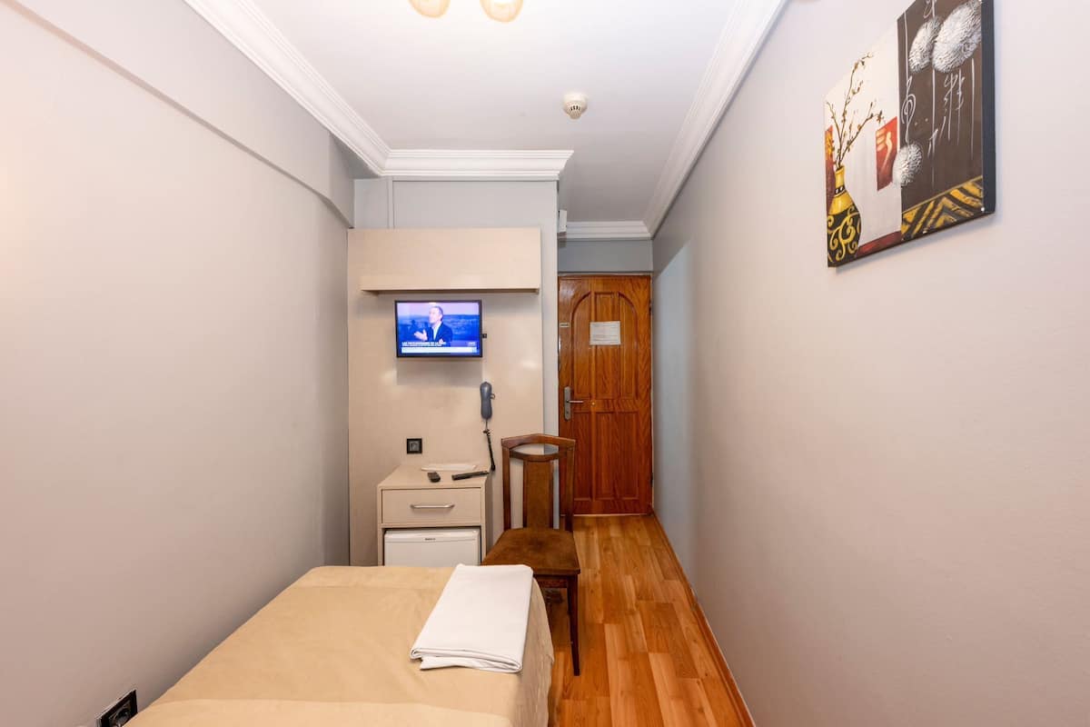 Habitación de hotel con cama, televisor montado en la pared, puerta de madera y una pequeña mesa con silla.