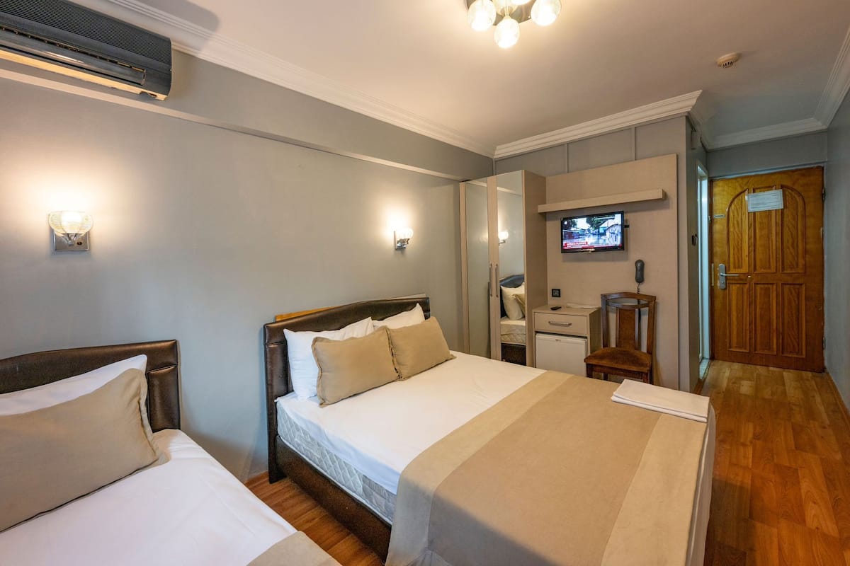 Una habitación de hotel con una cama grande, una mesita de noche, un espejo, un televisor y una puerta de madera.