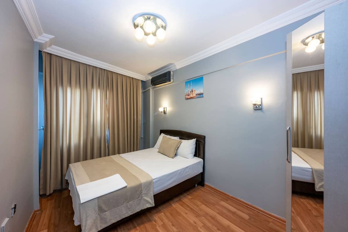 Una habitación de hotel con cama, cortinas, lámpara en el techo y aire acondicionado de pared.