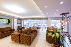 Un hall d’hôtel moderne doté d’un grand espace salon, d’un téléviseur et offrant une vue sur la rue grâce à de grandes fenêtres.