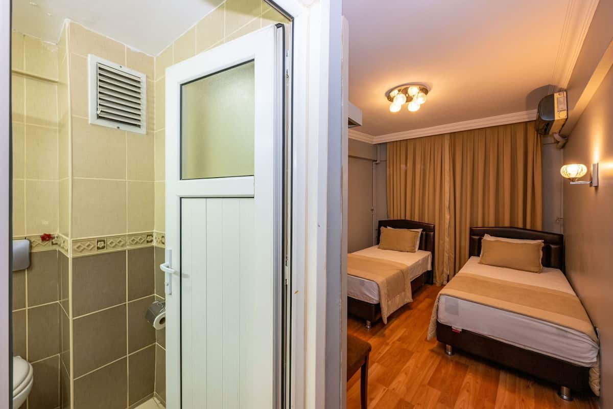 Habitación de hotel con ducha, dos camas, baño y suelo de madera.