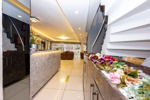 Un hall d’hôtel avec un comptoir d’accueil, un canapé et un arrangement floral.