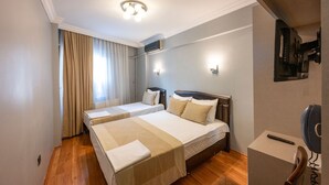 Habitación de hotel con dos camas, una lámpara en el techo, un equipo de aire acondicionado, un televisor y un control remoto sobre un atril.