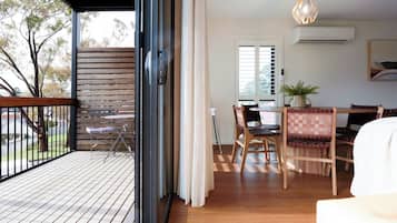 A room with a wooden deck, a dining area with a table and chairs, a potted plant, and an air conditioning unit.