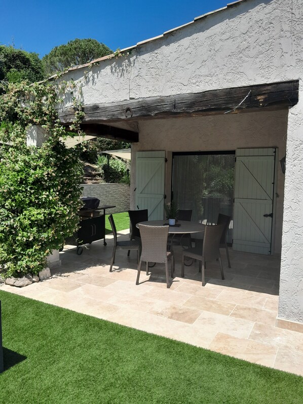 Eine Terrasse im Freien mit Tisch, Stühlen, einem Grill und einem überdachten Bereich mit einer Tür.