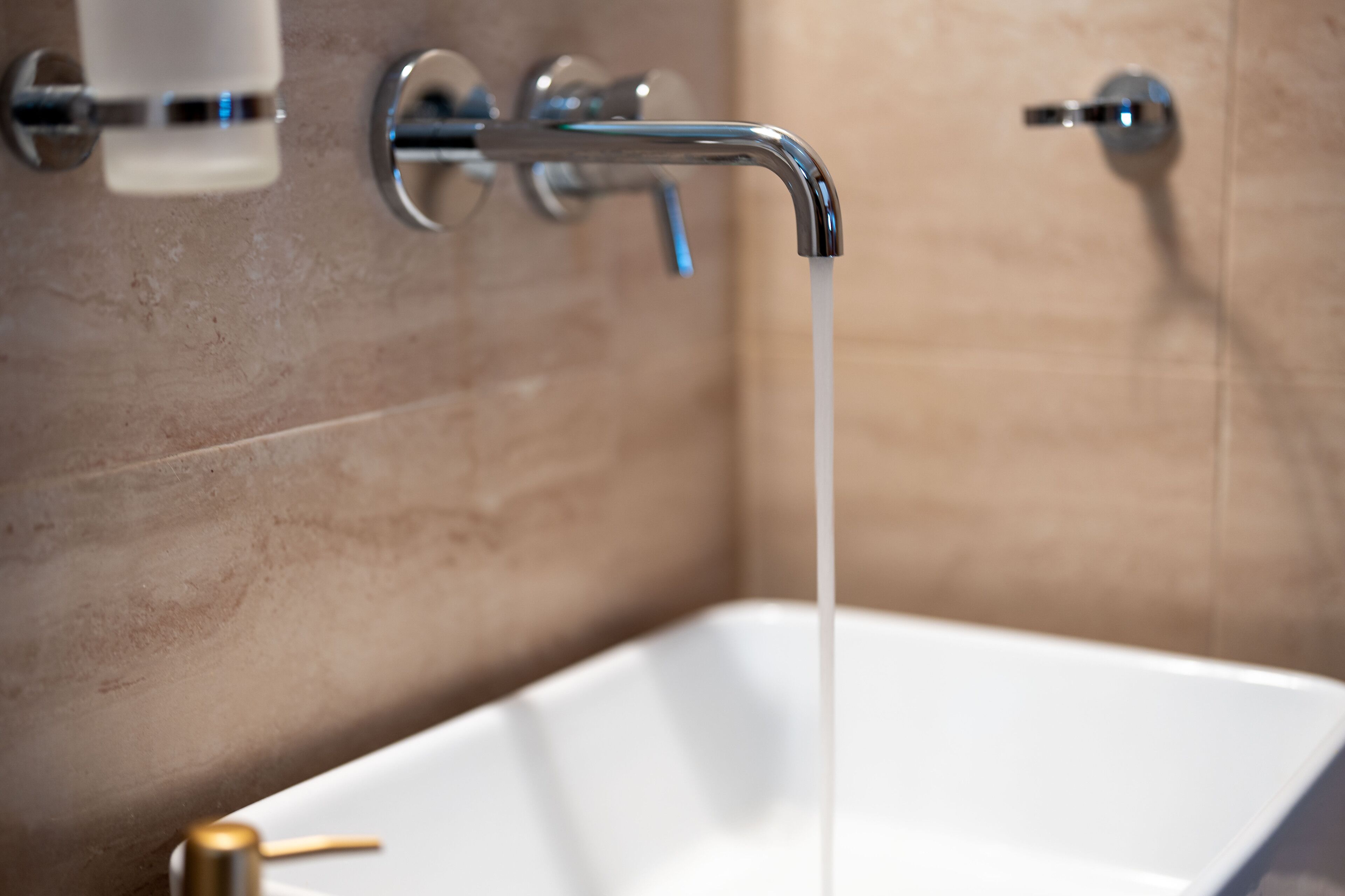 Un baño con una bañera blanca, un grifo de cromo y paredes de azulejos color beige.