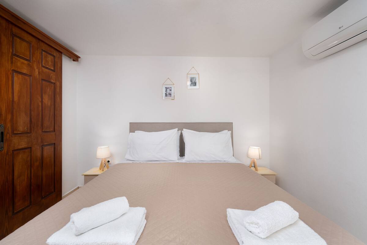 Una cama bien hecha con sábanas blancas, dos lámparas de noche y un armario de madera.