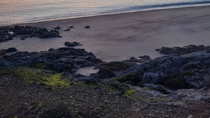 Ein Strand mit felsigem Vordergrund und ruhiger See.