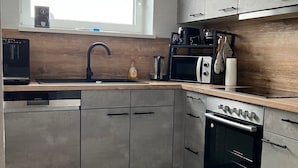 Une cuisine moderne avec des meubles gris, un four encastré, un four à micro-ondes et une machine à café.