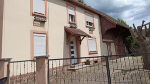 A two-story building with a tiled roof, a covered entrance, and a metal gate. - Village house  (Merxheim)