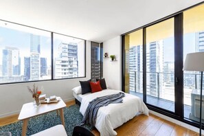 A modern bedroom with a large bed, a small table, and a view of a cityscape through large windows. - A Chic 2BR Apt, City Views Near Southern Cross (Melbourne)