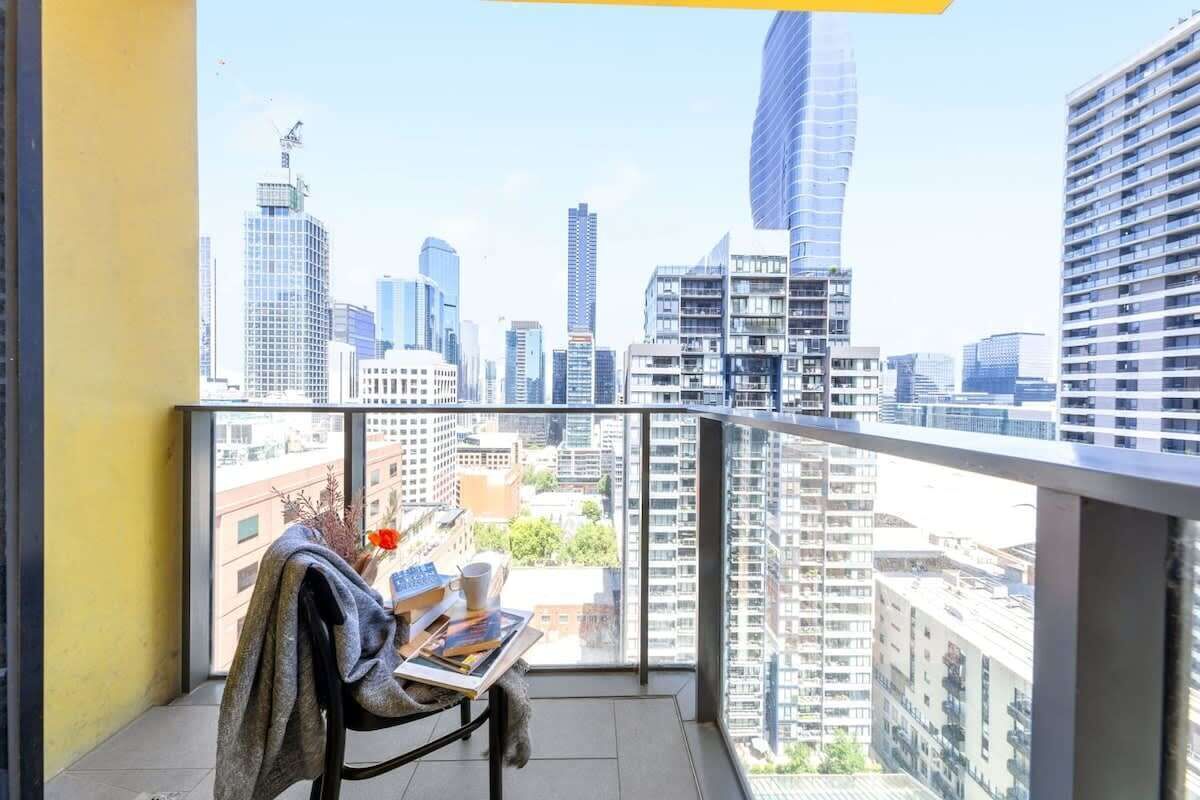 A balcony with a city view, a table with a book and a cup, and a chair with a blanket.