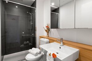 A modern bathroom with a glass-enclosed shower, a white sink, and a wooden vanity. - A Chic 2BR Apt, City Views Near Southern Cross (Melbourne)