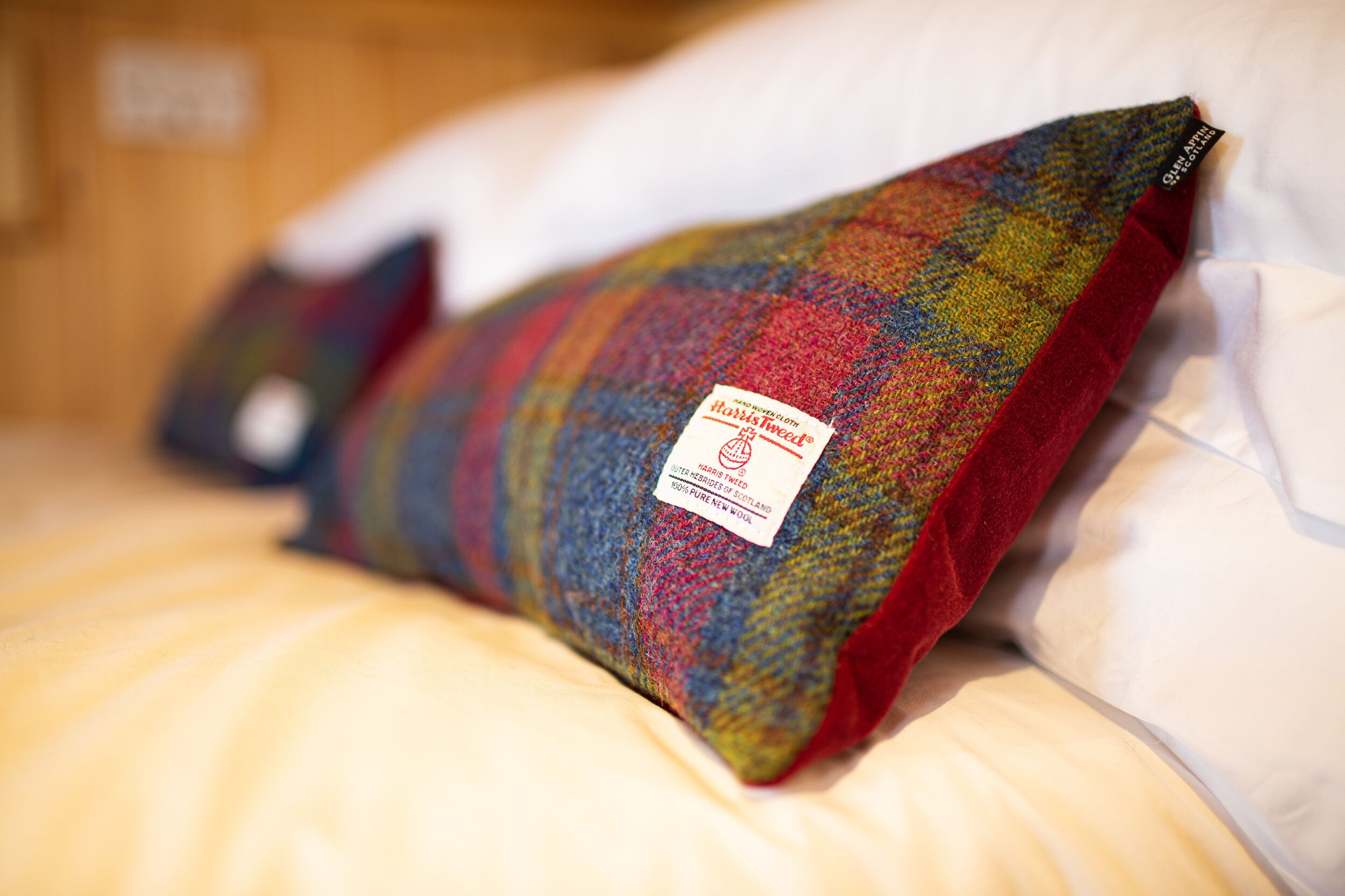 Almohada de cuadros sobre una cama, con una etiqueta que indica que es hecha a mano.