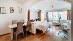 A modern hotel room with a dining area, a bed with a desk, and a view of the city. - Fitness friendly studio apartment in Paradiso (Little Paradise) (Paradiso)