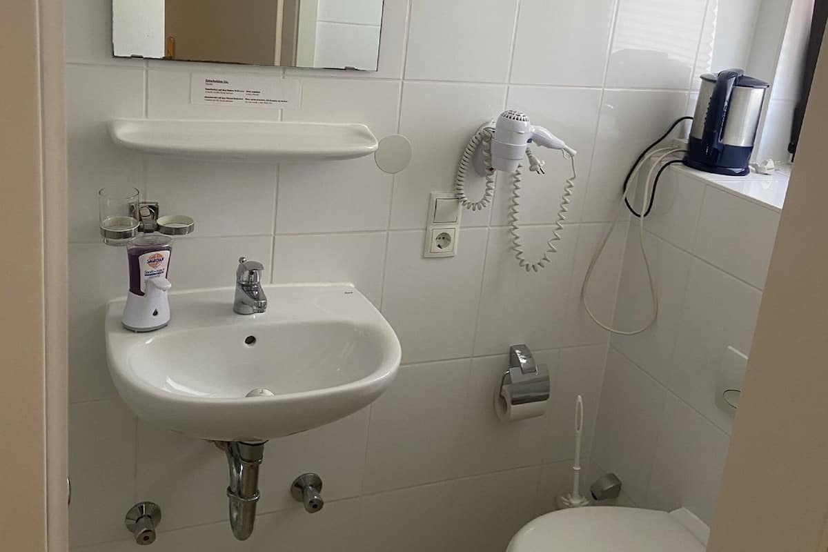 A small, clean bathroom with a white sink, mirror, and toilet. There is a towel rack above the sink and a hairdryer on the wall.