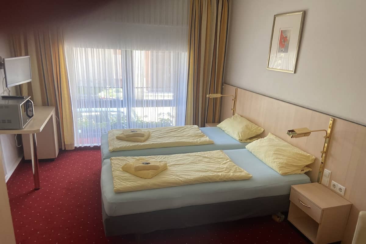 A hotel room with two beds, a desk, a chair, a bedside table, and a window with curtains.