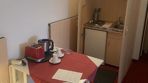 Una kitchenette compacta con una mesita, un mantel rojo, un tostador, un hervidor y un lavamanos.