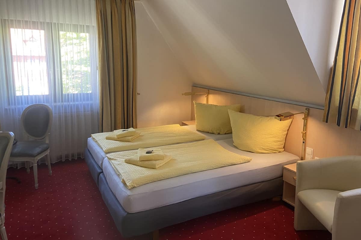 A hotel room with a bed, two pillows, a chair, a desk, and a window with curtains.