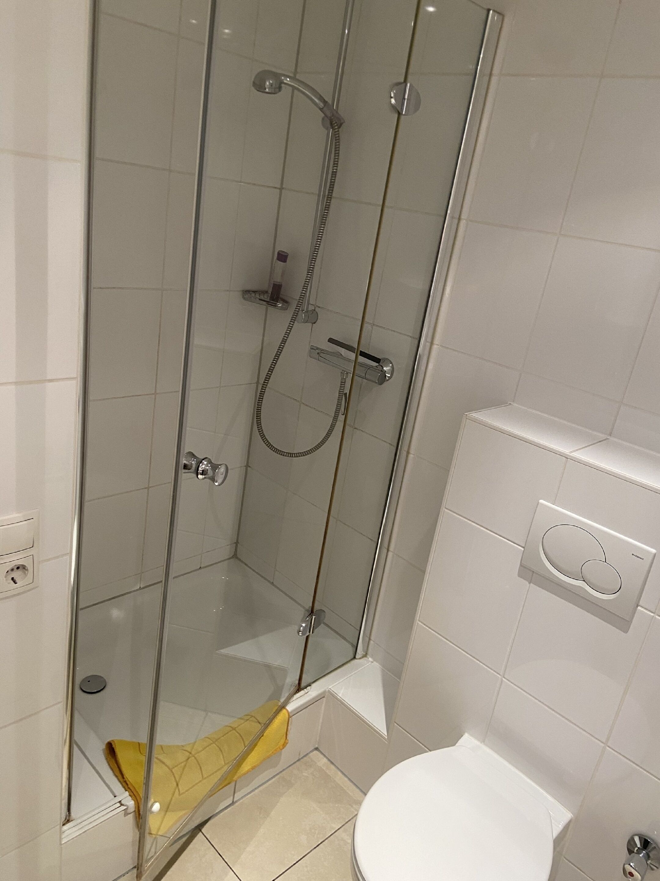 Un box de ducha con paredes de vidrio, una toalla amarilla y un inodoro blanco en el baño contiguo.