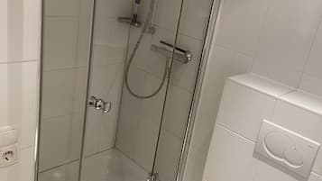 Un box de ducha con paredes de vidrio, una toalla amarilla y un inodoro blanco en el baño contiguo.