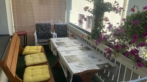 Un balcón con una mesa dispuesta para dos, dos sillas y un banco con cojines amarillos.