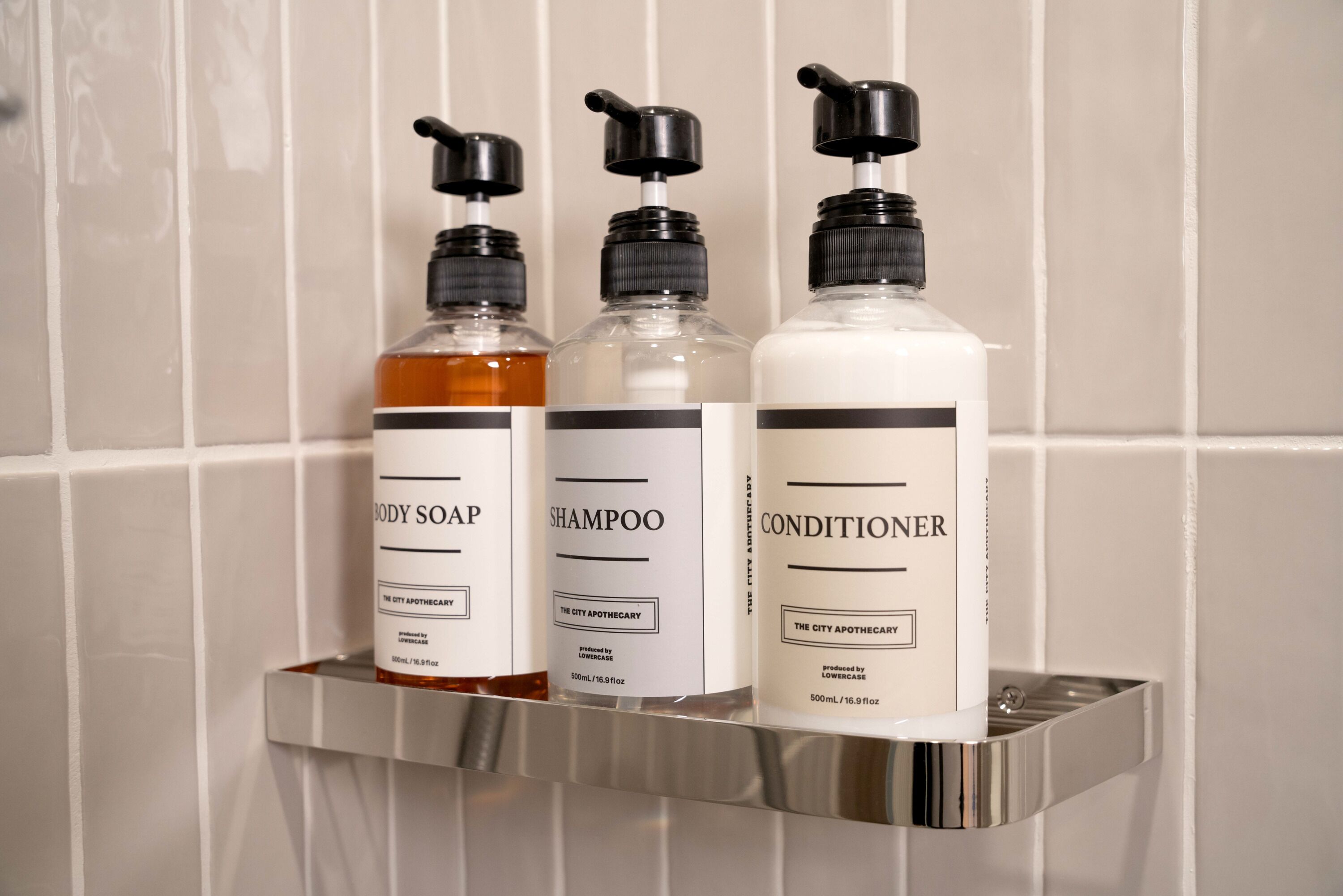 Trois flacons de produits de toilette sont posés sur une étagère métallique, devant un mur carrelé.