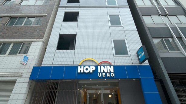 Un hôtel moderne, reconnaissable à son enseigne bien visible « HOP INN UENO » au-dessus de l’entrée.