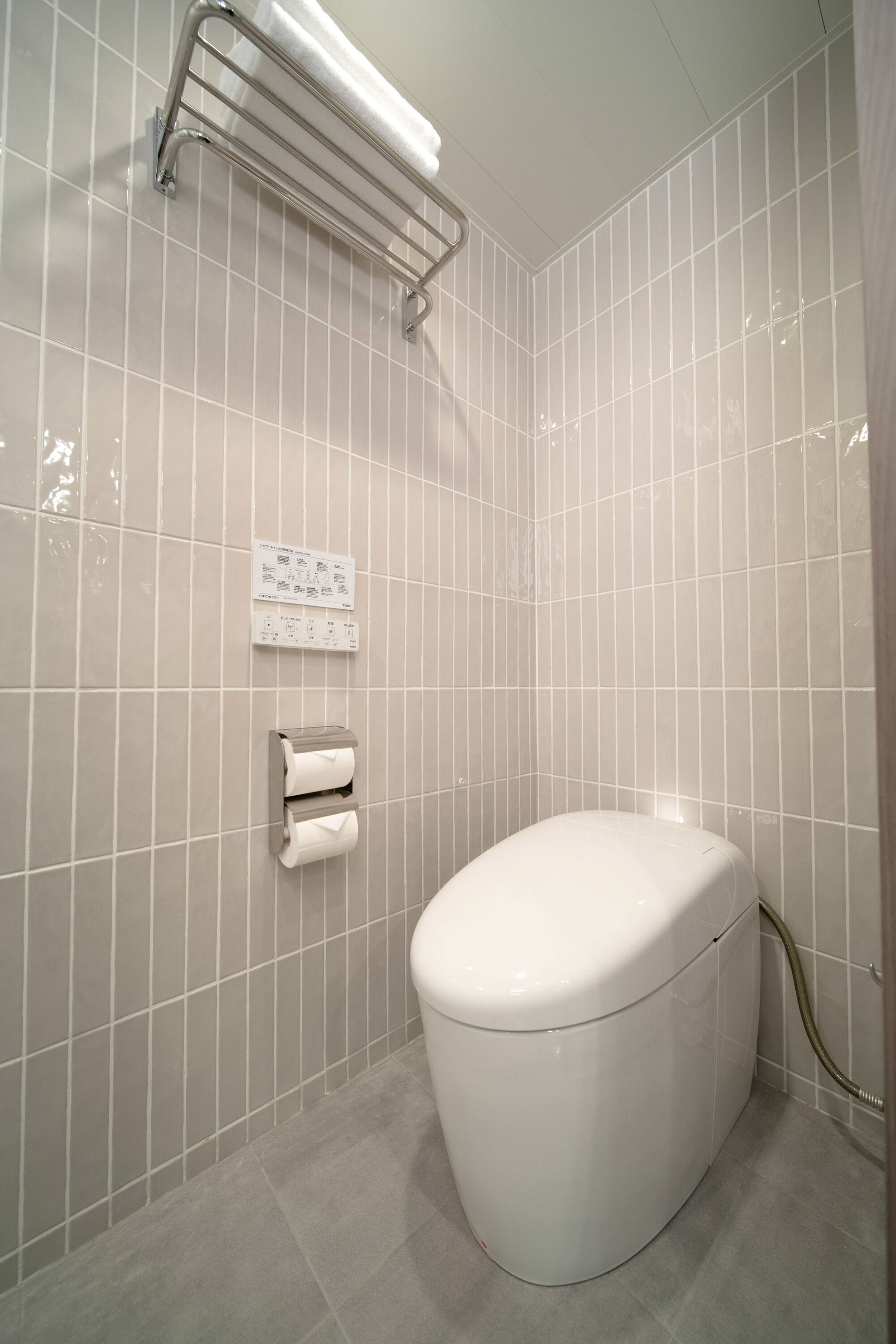 Casa de banho com sanita, suporte para toalhas e dispensador de papel.