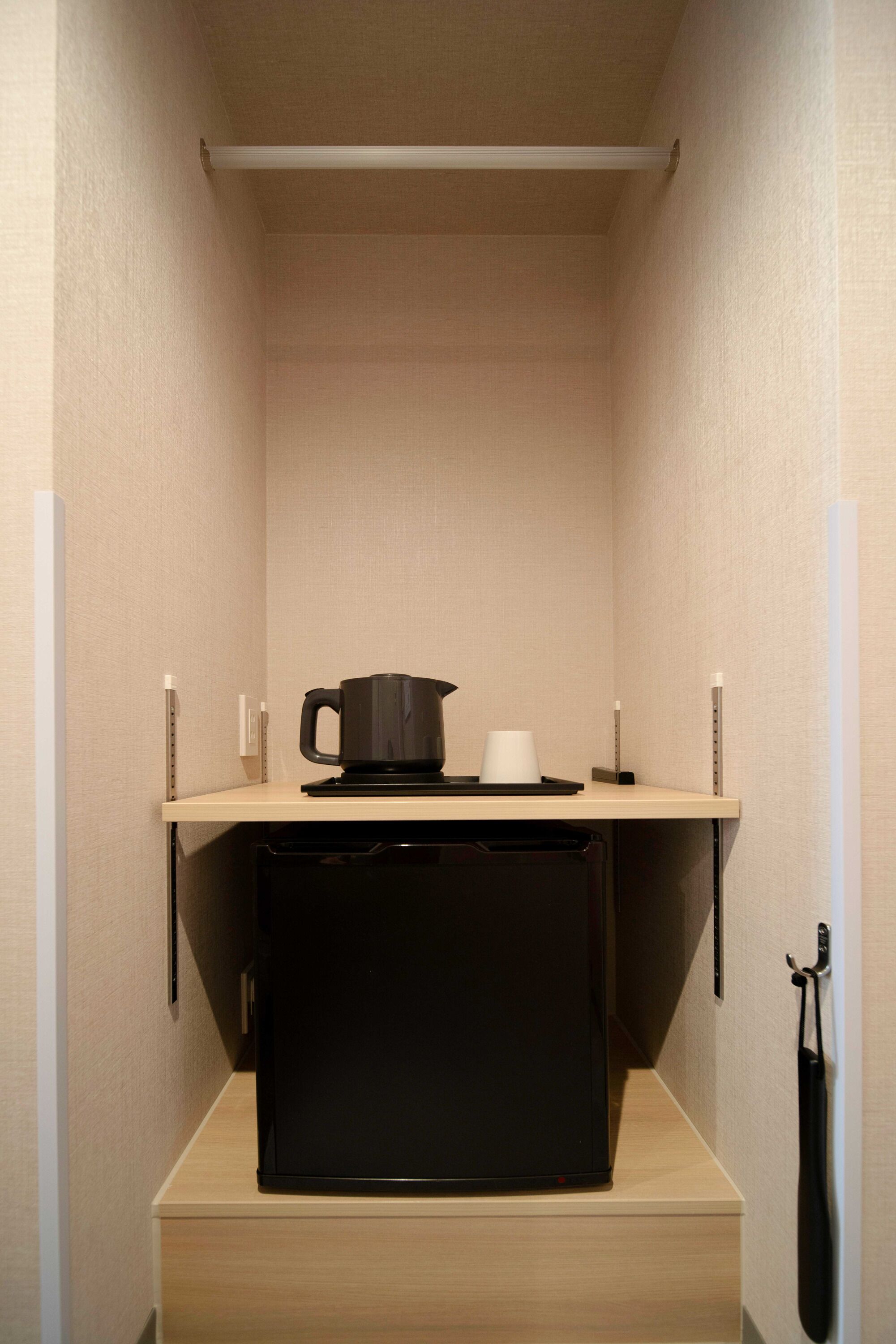 Una kitchenette compacta con un refrigerador negro, una cafetera y una taza sobre una pequeña encimera.