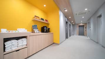 A hotel reception area with a bright yellow wall, a wooden reception desk, and a long hallway with doors.