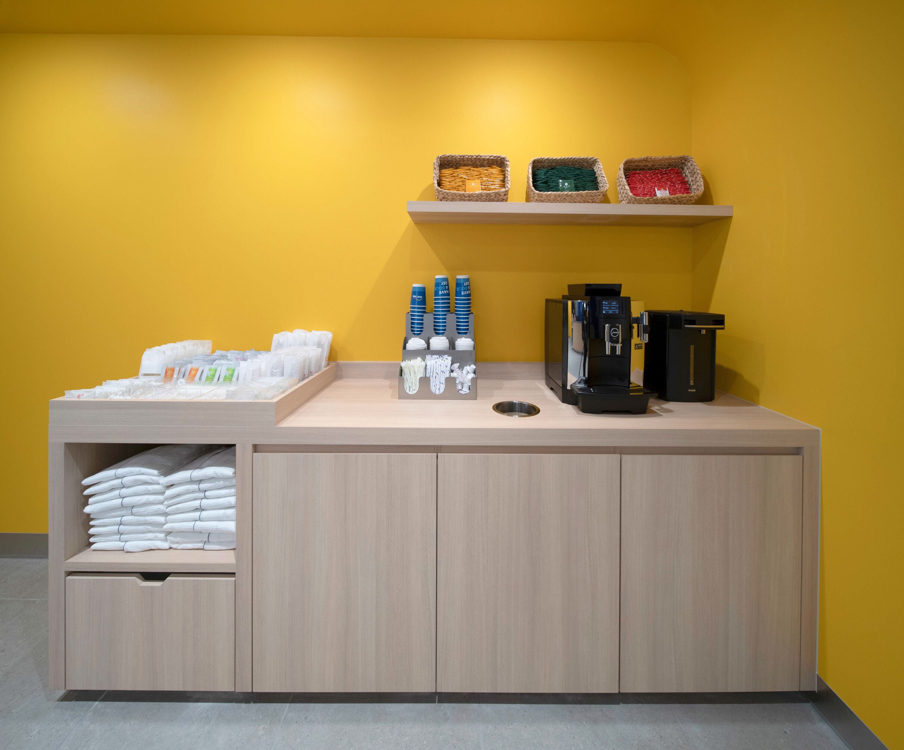 A hotel reception area with a counter, coffee machine, and storage shelves.