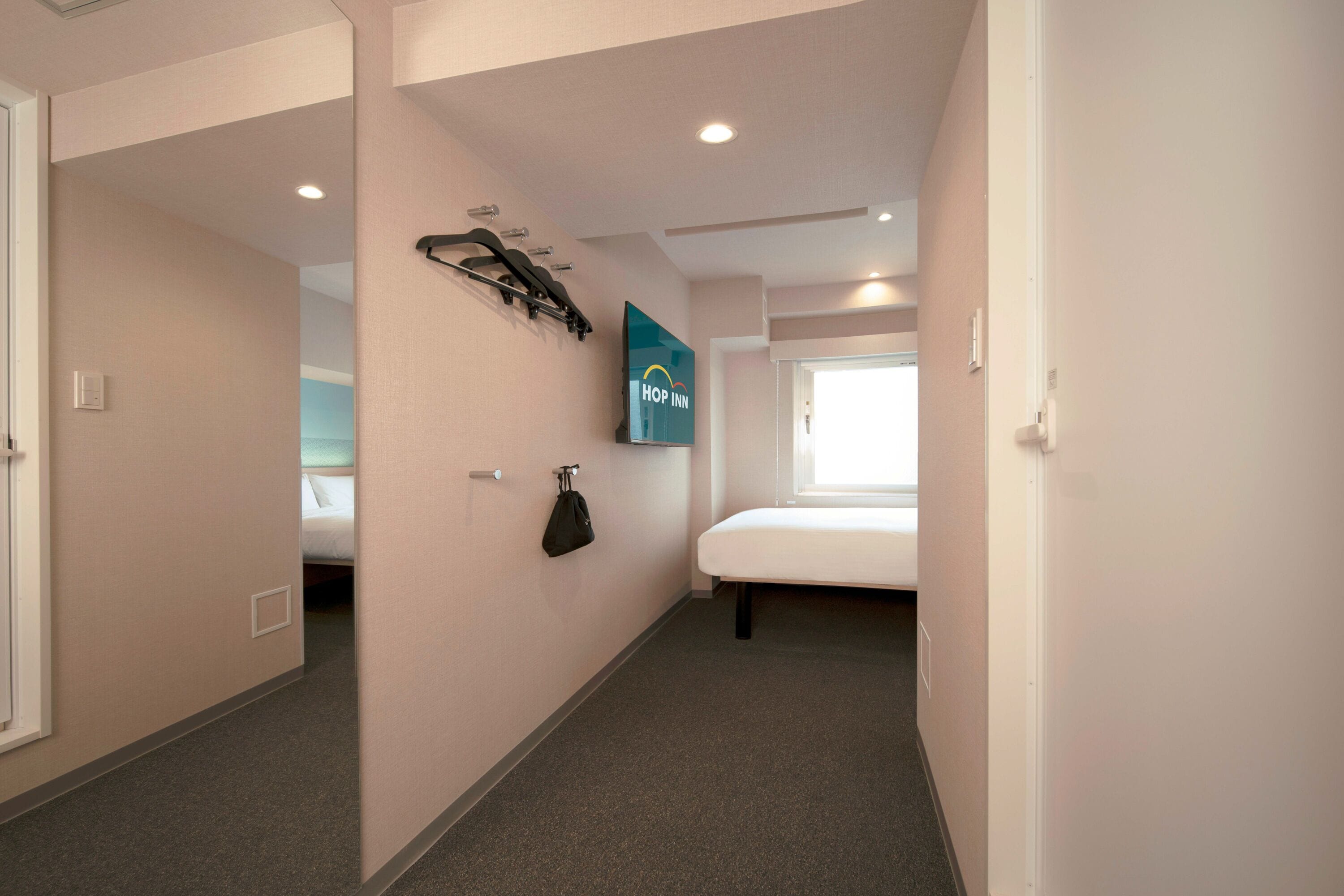 A hotel room with a bed, a TV mounted on the wall, and a coat rack.