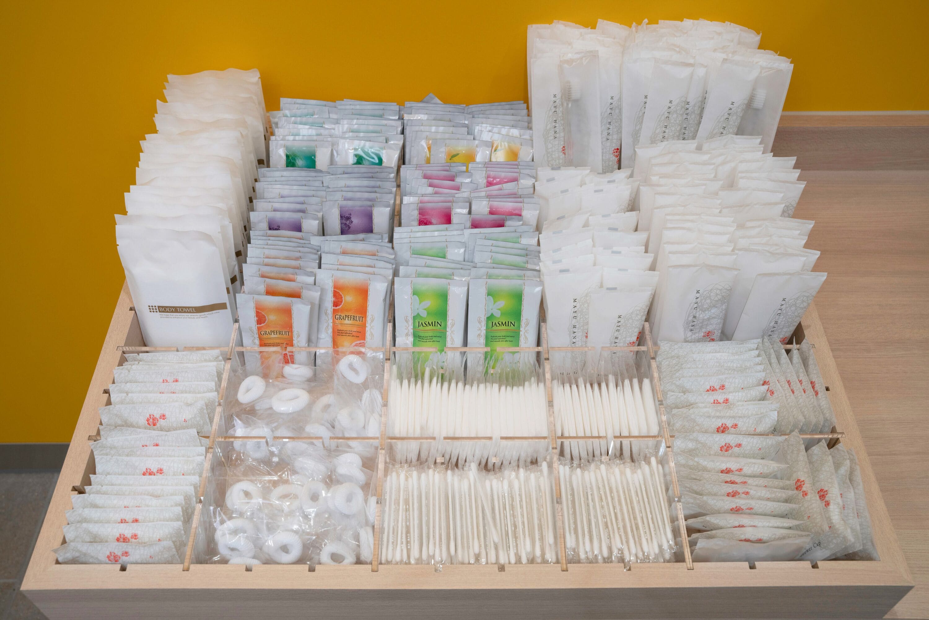 A display of various toiletries and personal care items organized in a wooden box against a yellow background.