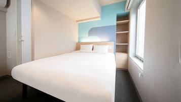 A hotel room with a large bed, a wardrobe, a built-in shelf unit, and a window with blinds.