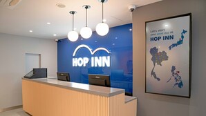 Un comptoir d’accueil avec une enseigne « Hop Inn », une carte du Japon et un message de bienvenue.