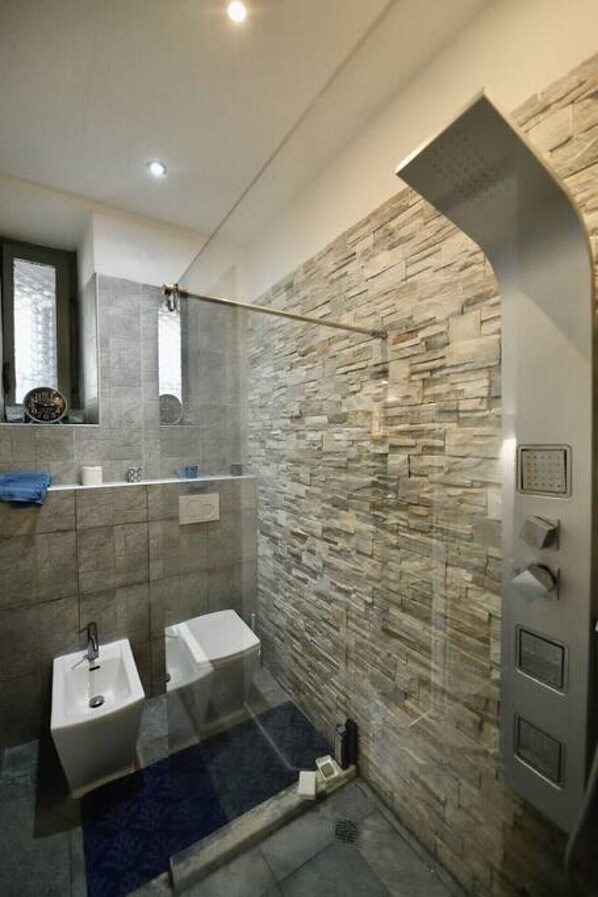 A modern bathroom with a stone wall, a shower, and two sinks. - THE 150 HOME - Elegant flat - Colosseum (Roma)