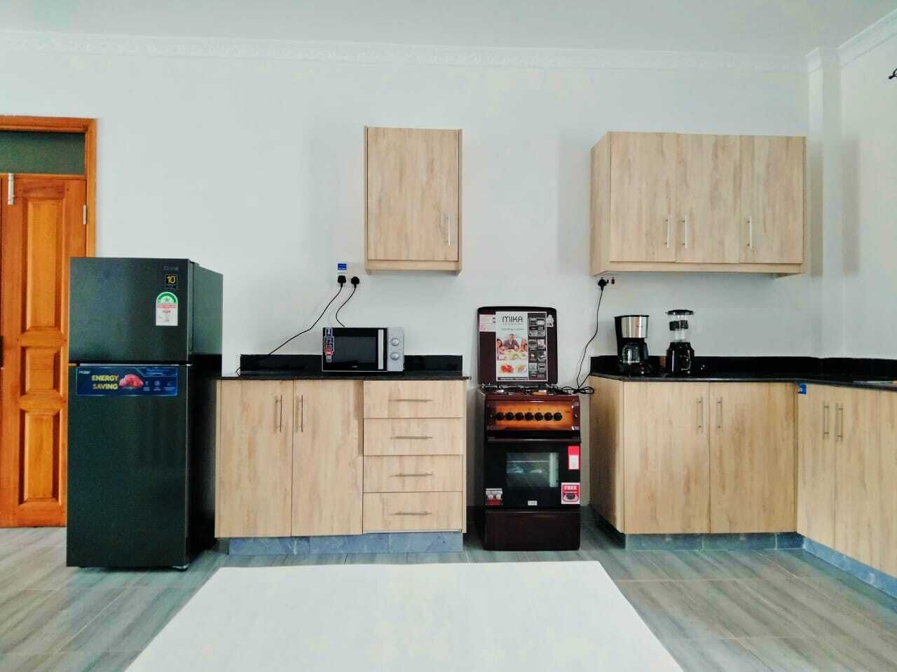 Een keuken met houten kastjes, een koelkast, een magnetron, een koffieapparaat en een klein oven.