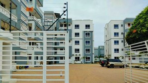 Un complexe résidentiel sécurisé, doté de plusieurs étages et de balcons, d’une cour pavée et d’un parking pour véhicules.