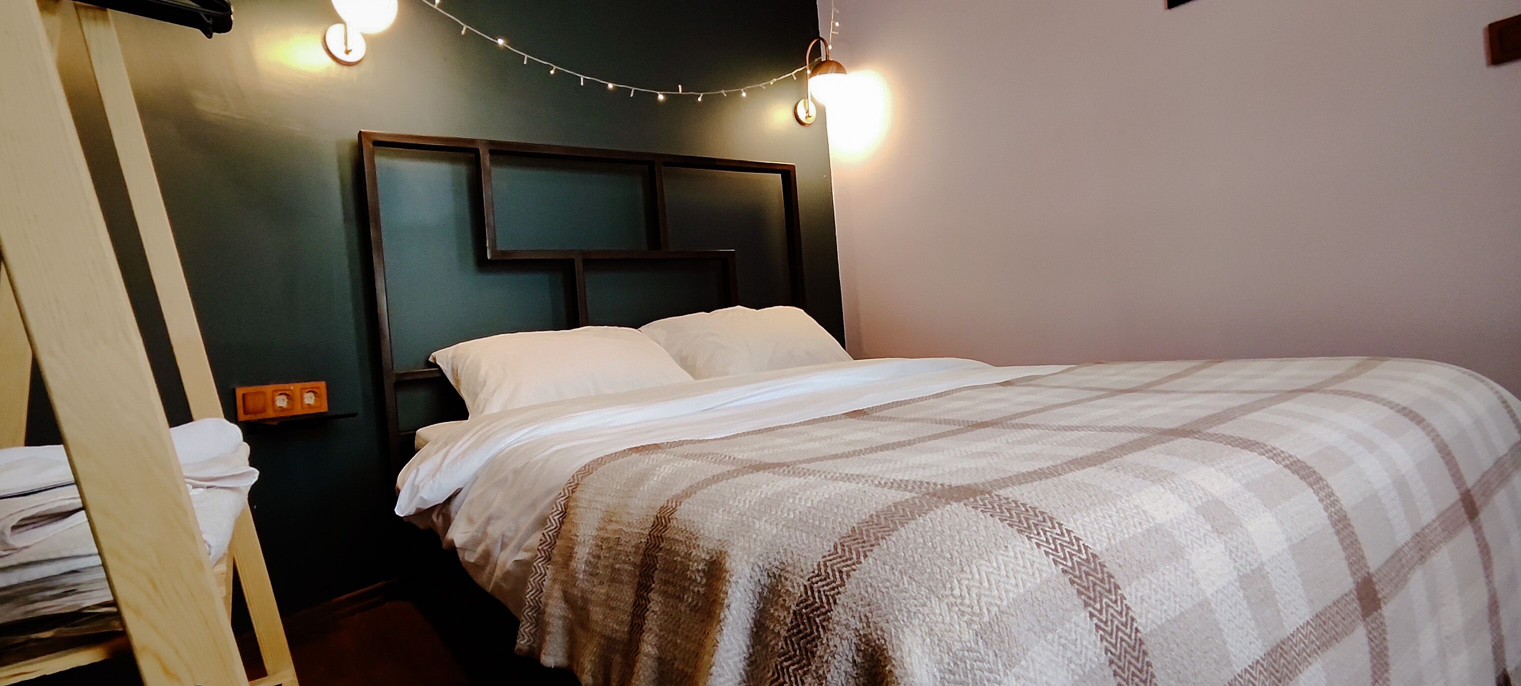 A neatly made bed with a checkered blanket, a headboard with built-in lighting, and a small nightstand with a lamp.