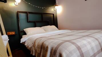 A neatly made bed with a checkered blanket, a headboard with built-in lighting, and a small nightstand with a lamp.