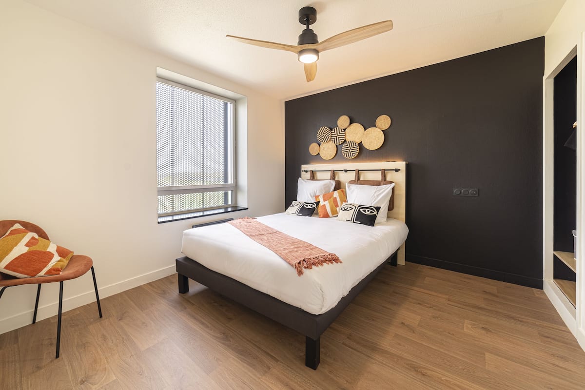 Une chambre à coucher avec un lit, une chaise, une fenêtre et un ventilateur de plafond.