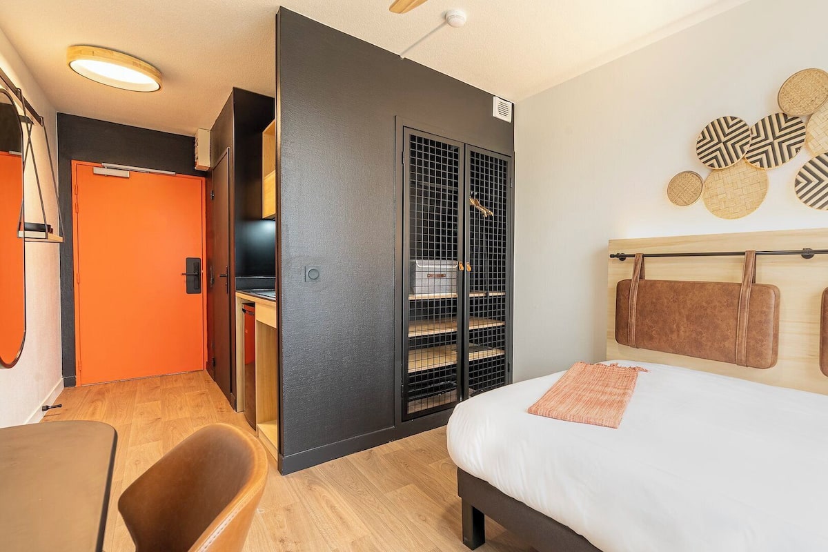 Une chambre d’hôtel comprenant un lit, un bureau, une chaise, une armoire et un mur décoré.