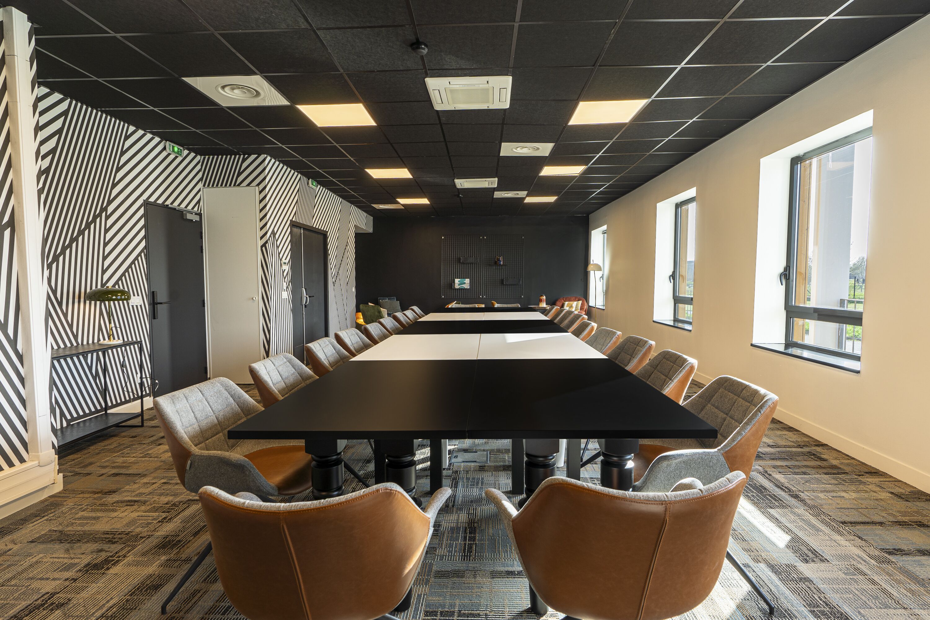 Une salle de conférence dotée d’une longue table, de fauteuils en cuir, de murs décorés de motifs et de grandes fenêtres.